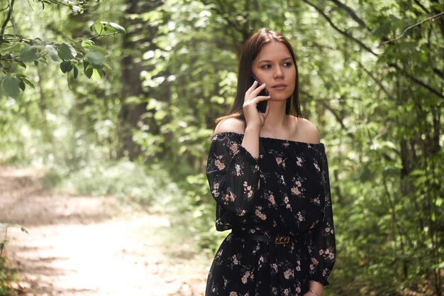 Schönes Mädchen, das im sonnigen Waldpark telefoniert