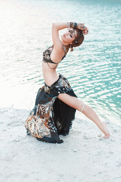 Schönes Mädchen, das im Stammesstil auf weißem Sandstrand nahe dem Wasser tanzt