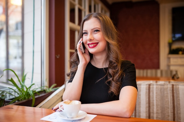 Schönes Mädchen, das Kaffee trinkt und am Telefon spricht