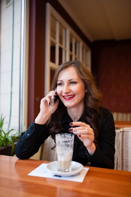 Schönes Mädchen, das Kaffee trinkt und am Telefon spricht