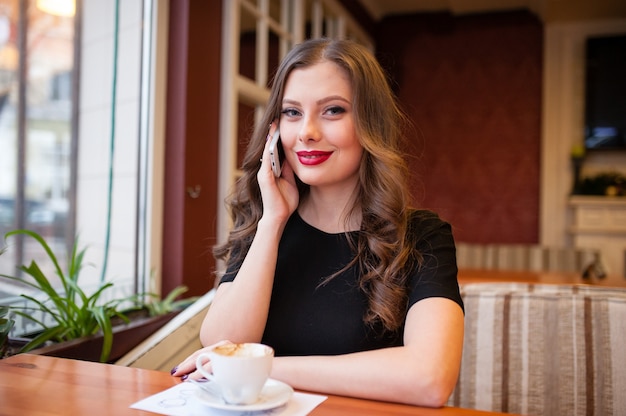 Schönes Mädchen, das Kaffee trinkt und am Telefon spricht