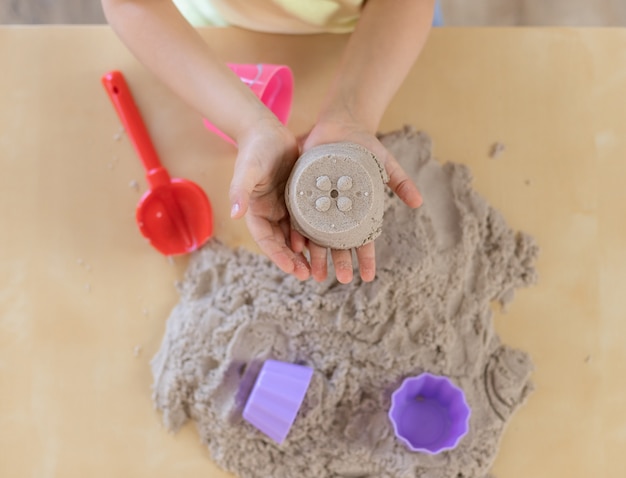 Schönes Mädchen, das mit kinetischem Sand zu Hause spielt