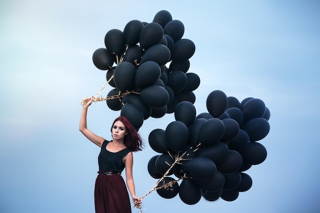 Schönes Mädchen, das mit schwarzen Ballons geht