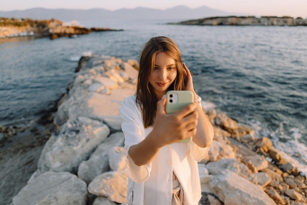 Foto schönes mädchen, das selfies auf ihrem handy in der nähe des meeres und der berge macht