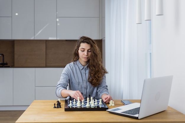 Schönes Mädchen, das zu Hause sitzt und Schach online mit einem Laptop spielt