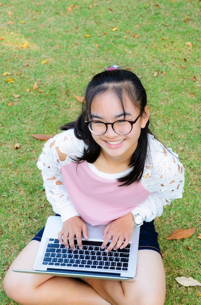 Schönes Mädchen freut sich mit einem Laptop auf dem Rasen im Park