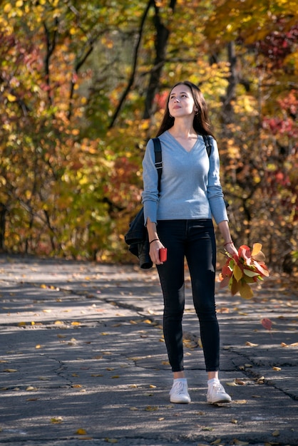 Schönes Mädchen geht entlang der Gasse des Herbstparks. Junge nachdenkliche Frau im Wald. Vertikaler Rahmen.