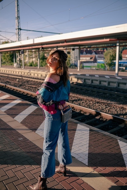 Schönes Mädchen im 90er-Jahre-Stil mit tragbarem Radioempfänger in der Hand posiert auf dem Bahnsteig des Bahnhofs