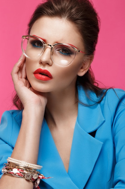 Schönes Mädchen im blauen Anzug auf rosa Hintergrund mit kreativem Make-up und modischem Stil.