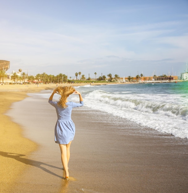 Schönes Mädchen im blauen Kleid geht am Strand Erstaunliches Sommerfoto Frau in der Nähe des Meeres Fröhliche und lustige Emotionen Urlaubsreisekonzept Schlanke Beine Warmes Meerwasser