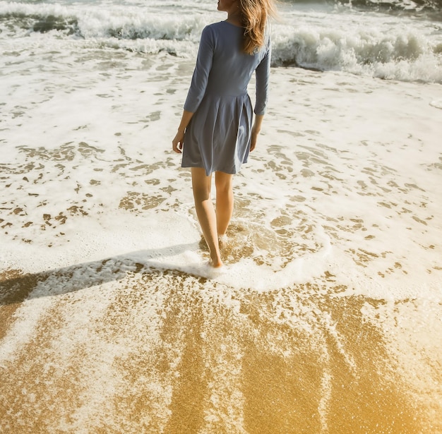 Schönes Mädchen im blauen Kleid geht am Strand Erstaunliches Sommerfoto Frau in der Nähe des Meeres Urlaubsreisekonzept Schlanke Beine Warmes Meerwasser