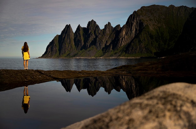 schönes mädchen im gelben kleid bewundert mächtige berge, magische spiegelung im wasser, norwegen, senja