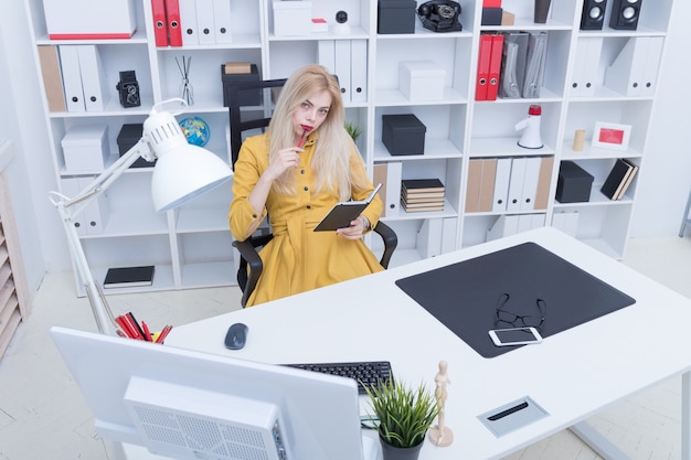 Schönes Mädchen im gelben Kleid, das an ihrem Arbeitsplatz arbeitet