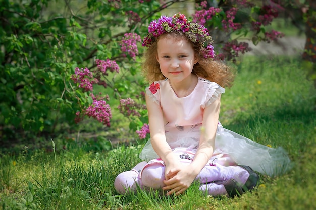 Schönes Mädchen im Kranz von Flieder gegen Hintergrund des Busches mit lila Blumen.