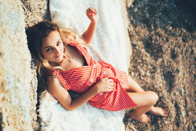 Schönes Mädchen im roten Kleid, das auf einem Felsen nahe dem Sand liegt