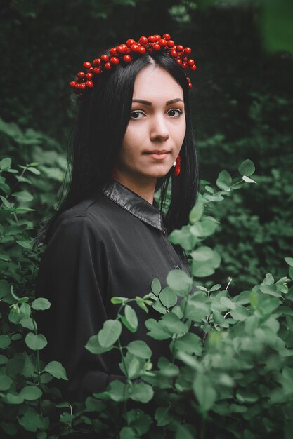 Schönes Mädchen im schwarzen Kleid und roten Ohrringen auf dem Hintergrund des Waldes.