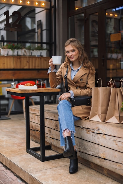 Schönes Mädchen im Trenchcoat und in den Jeans verträumt