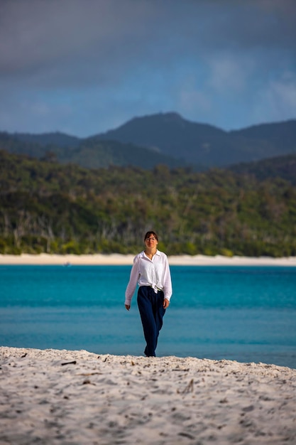 Schönes Mädchen im weißen Hemd geht am Strand von Whitehaven bei Sonnenaufgang, Whitesunday Islands, Australien