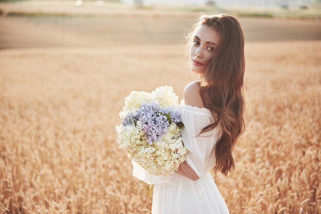 Schönes Mädchen im weißen Kleid, das auf dem Herbstfeld des Weizens zur Sonnenuntergangszeit läuft.