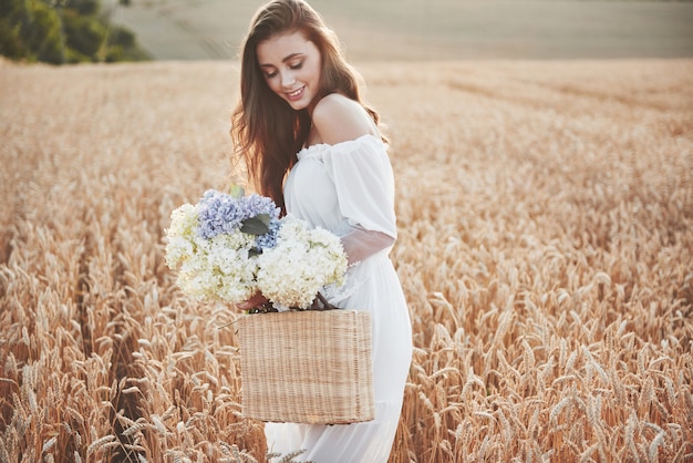 Schönes Mädchen im weißen Kleid, das auf dem Herbstfeld des Weizens zur Sonnenuntergangszeit läuft.