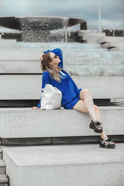 Schönes Mädchen in einem blauen Anzug für einen Spaziergang in der Nähe des Stadtbrunnens