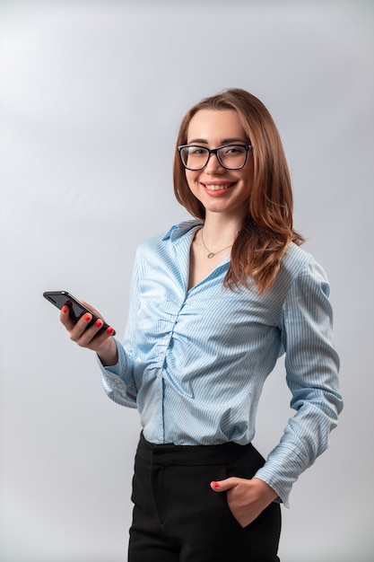 schönes Mädchen in einem blauen Hemd und in der Brille mit einem Telefon auf einem weißen Hintergrund.