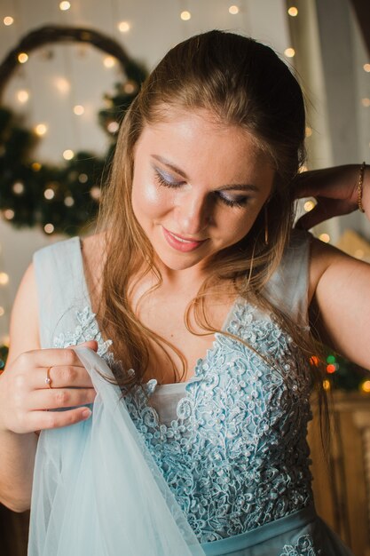 Schönes Mädchen in einem blauen Kleid vor dem Hintergrund eines Weihnachtsbaums und der Lichter des neuen Jahres