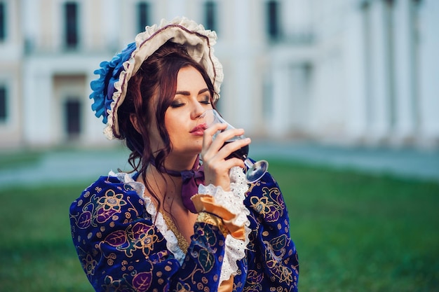 Schönes Mädchen in einem blauen Vintage-Kleid trinkt Wein