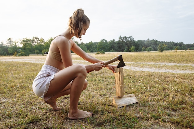Schönes Mädchen in einem Campingdorf hackt Brennholz mit einer Axt für einen Grill