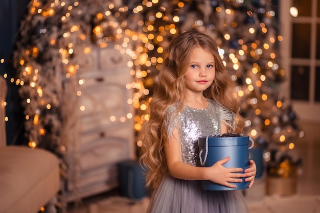 Schönes Mädchen in einem eleganten Kleid vor dem Hintergrund von Weihnachtsbeleuchtung und einem Weihnachtsbaum in einem schönen Interieur