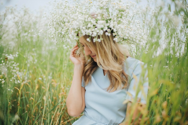 schönes Mädchen in einem Feld von Gänseblümchen. Mädchen in einem Strohhut und einem blauen Kleid. Kamillenfeld im Sommer