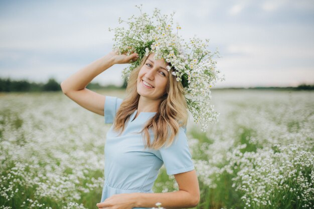 schönes Mädchen in einem Feld von Gänseblümchen. Mädchen in einem Strohhut und einem blauen Kleid. Kamillenfeld im Sommer