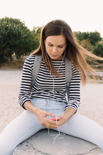 Schönes Mädchen in einem gestreiften T-Shirt hörend Musik auf dem Strand