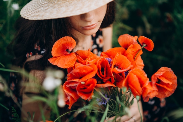 Schönes Mädchen in einem Hut im Gras mit einem Strauß roter Mohnblumen. Draufsicht Porträt.