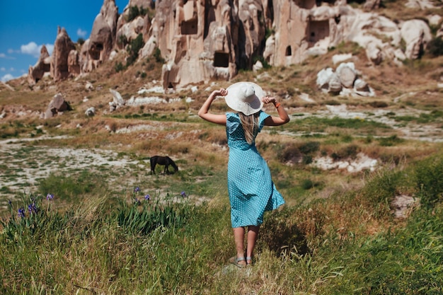 Schönes Mädchen in einem Hut und einem türkisfarbenen Kleid betrachtet die Berge von Kappadokien