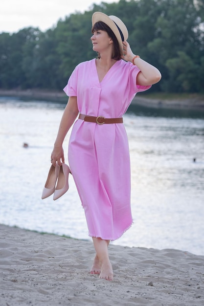 schönes Mädchen in einem rosa Kleid am Strand in der Nähe des Flusses