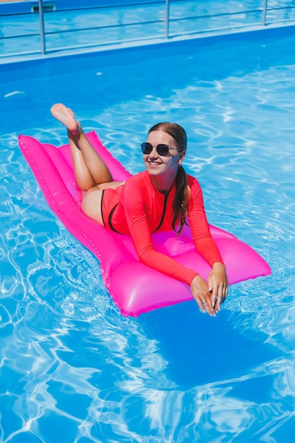 Schönes Mädchen in einem rosafarbenen Badeanzug, das sich auf einer aufblasbaren rosafarbenen Matratze im Pool entspannt Eine schlanke, heiße Frau mit Sonnenbrille und Badeanzügen sonnt sich Eine Frau entspannt sich in einem Luxusresort