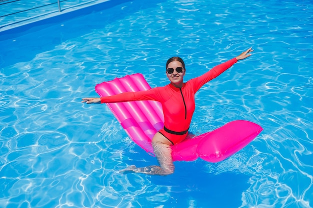 Schönes Mädchen in einem rosafarbenen Badeanzug, das sich auf einer aufblasbaren rosafarbenen Matratze im Pool entspannt Eine schlanke, heiße Frau mit Sonnenbrille und Badeanzügen sonnt sich Eine Frau entspannt sich in einem Luxusresort