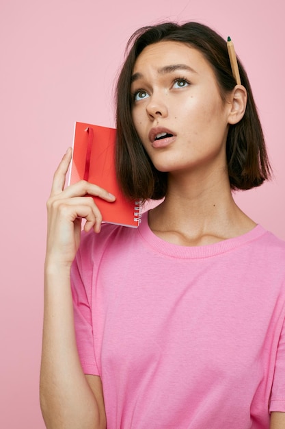 Schönes Mädchen in einem rosafarbenen T-Shirt, rotem Notizbuch und Stift Lifestyle unverändert