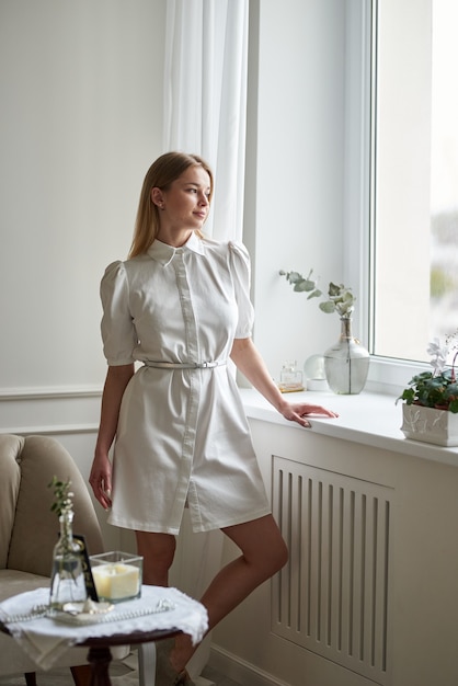 Schönes Mädchen in einem Sommerkleid steht am Fenster