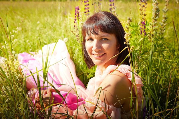 Schönes Mädchen in einem üppigen rosafarbenen Ballkleid im grünen Feld während des Blühens der Blumen