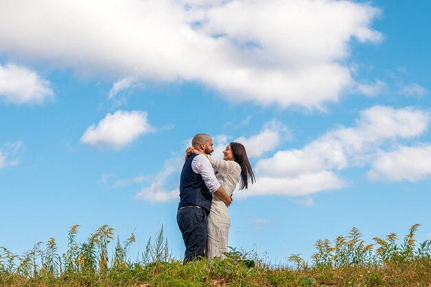 Schönes Mädchen in einem weißen Kleid und ein Typ auf einem Feld vor blauem Himmel mit Wolken