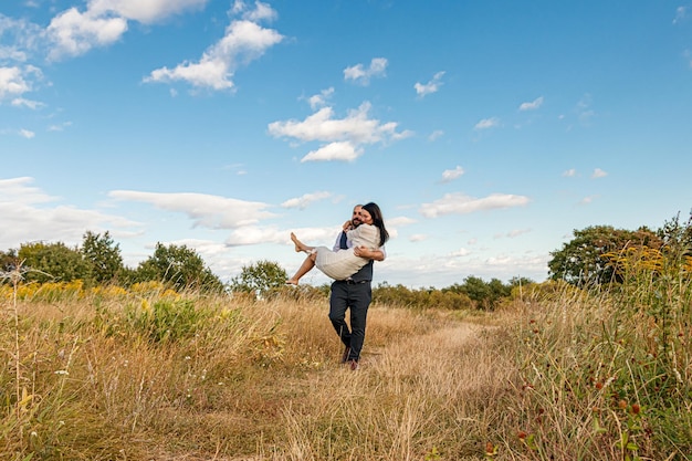 Schönes Mädchen in einem weißen Kleid und ein Typ auf einem Feld vor blauem Himmel mit Wolken