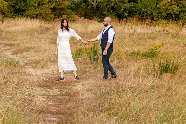 Schönes Mädchen in einem weißen Kleid und ein Typ auf einem Feld vor blauem Himmel mit Wolken