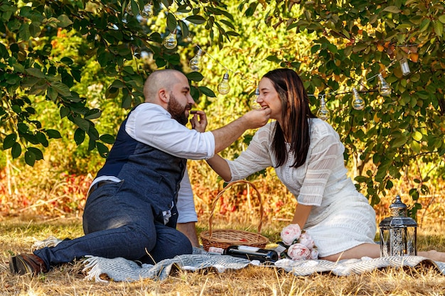 Schönes Mädchen in einem weißen Kleid und ein Typ liegen auf einer Lichtung bei einem Picknick