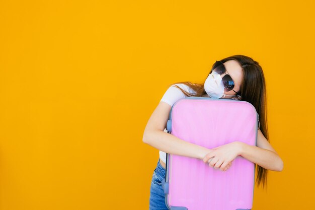 Schönes Mädchen in einem weißen Sommerkleid mit einem Koffer Medizinische Maske im Gesicht Geschlossene Grenzen