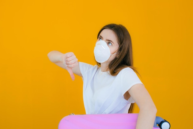 Schönes Mädchen in einem weißen Sommerkleid mit einem Koffer Medizinische Maske im Gesicht