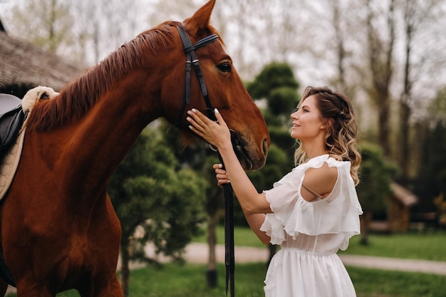 Schönes Mädchen in einem weißen Sommerkleid neben einem Pferd auf einer alten Ranch