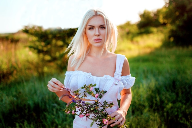 schönes Mädchen in einem zarten rosa Overall mit einem Strauß Wildblumen.