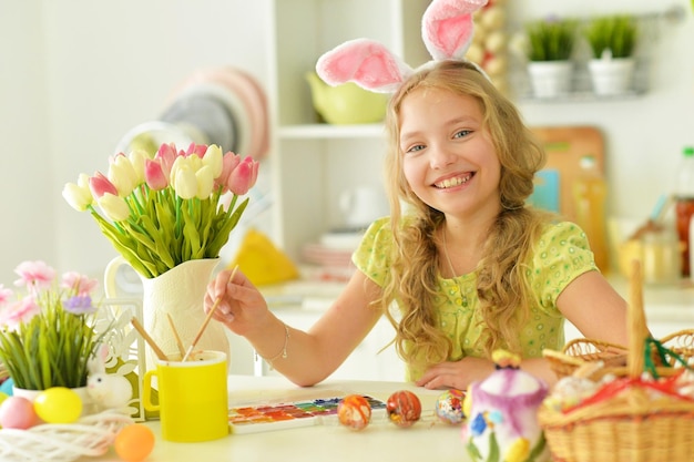 Schönes Mädchen in Hasenohren, das Eier für die Osterferien malt